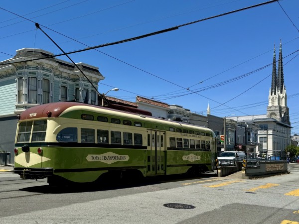 An old MUNI rail car on Church Street. The car is on rails and under an electric wire. It looks old, but well maintained and has a green and yellow color scheme. 