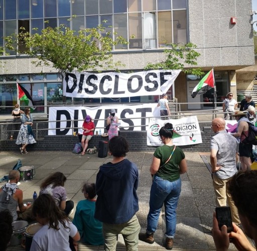 Giant banners reading DISCLOSE DIVEST hanging from a building, with protesters carrying flags