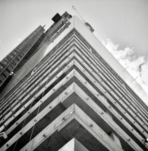 A black and white film photo. Looking straight up at the corner of a building under construction where half the glass has been installed and the other half shows the concrete frame in downtown Austin, Texas. Tuesday, March 19, 2024.