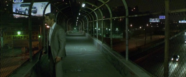 A still from the film Collateral by Michael Mann. It features Tom Cruise’s character looking over a highway from a pedestrian overpass. The visual tone of the still is cool greyish greens.
