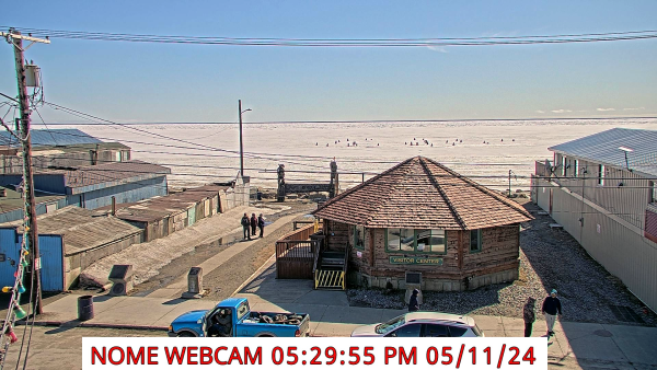 Webcam image looking south overlooking the Nome Visitor Center to Norton Sound with sea ice in the mid-frame and blue skies above. 