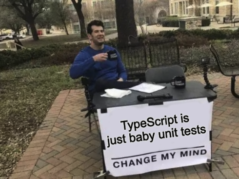 Change my mind meme with guy sitting at table outside with a banner attached that says "TypeScript is just baby unit tests change my mind" on it.