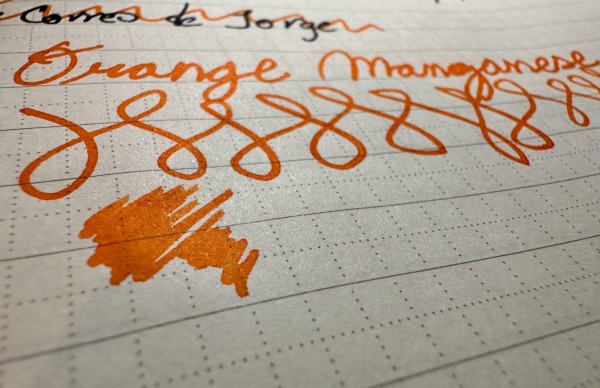 Close-up of handwriting in orange ink on lined paper, with a smudge of orange ink at the bottom.