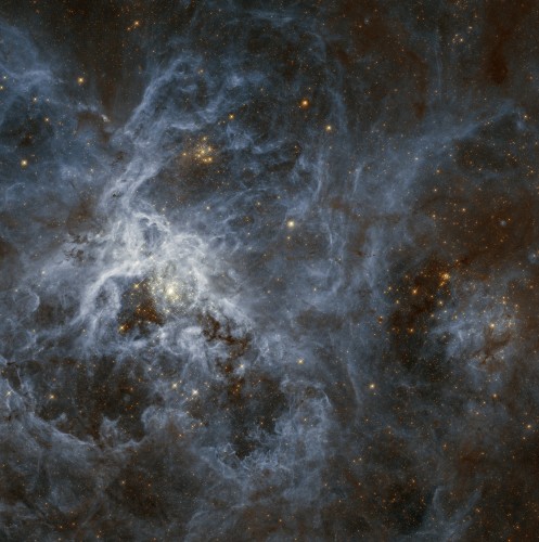 An incomprehensibly jumbled mess of clouds and stars. There is one prominent bright cluster left of center, and a few other clusters scattered about. The stars are a warm orange and yellow color while the clouds of dust and gas are pale blue. There are some darker ruddy brown areas where the dust is thicker.