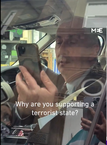 Picture of Hoyle aiming his phone at protestsrs (you can see a Palestinian flag reflected in the window).  Text reads 
Why are you supporting a terrorist state?