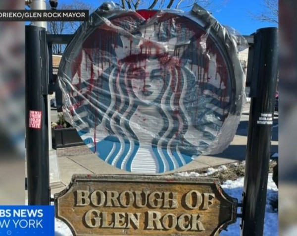 A Starbucks store sign in Glen Rock, NJ is pictured covered in red paint. There are two anti colonial stickers stuck to the signs posts. 