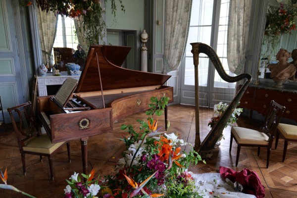 Le salon de musique, avec un piano et une harpe, avec au premier plan des fleurs