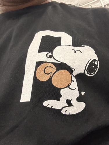 The image shows a graphic of the animated character Snoopy on a black T-shirt. Snoopy is leaning against a large letter "P." wearing boxing gloves 