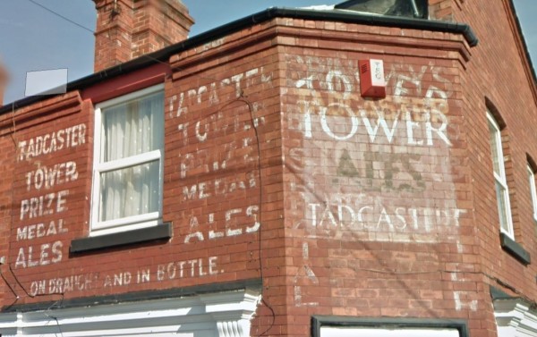 First floor of a corner building on a red-brick terrace. The wall either side of the window has fading signs painted in white with the same copy: 'Tadcaster Tower prize medal ales'. Underneath this, running along the length of the wall below the window, is written 'on draft and in bottle'.

To the right of these signs is the splay wall which has a layering up of fading painted signs all visible simultaneously: a palimpsest. Words that can be made out include: Tower; Tadcaster; and Ales.