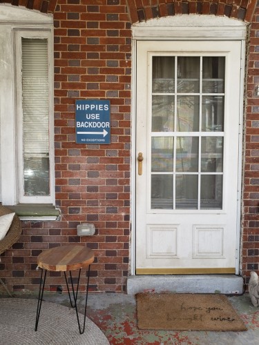 Image of porch and front door with sign reading "Hippies Use Backdoor - No Exceptions"