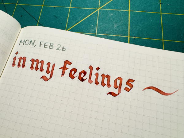 A notebook page with the words “in my feelings” written in large, blocky calligraphy using a deep dusty rose ink color