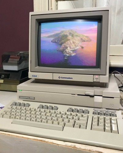 A photo of a Commodore 128D with a 1084 monitor on top, and a picture of Catalina island at sunrise on the screen. It's all very beige except for the colourful screen.