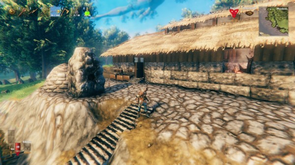 Screenshot from the game Valheim.

It shows my character standing on a set of stairs leading up to the new house. The building is low, with walls made of three rows of stone topped by wood and a thatch roof that has a raised part to let out the smoke from the hearth inside. 

One window shows part of a portal and other things in the interior.

The front of the house is paved, and that's also where the killn and the smelter sit for processing ore.

It is a sunny day in the Meadows, with lush trees in the background and a branch of Yggdrasil floating in the sky.