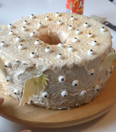An Angel food cake, with skin-textured frosting and covered with eyes & wings