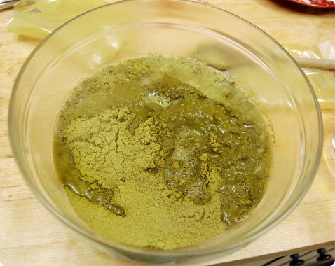 Henna powder mixed with a little liquid in a glass bowl.