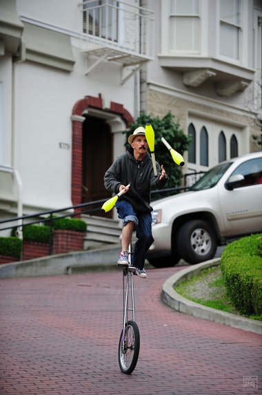 a man juggling neon yellow pins while riding a unicycle down a famously steep and winding road