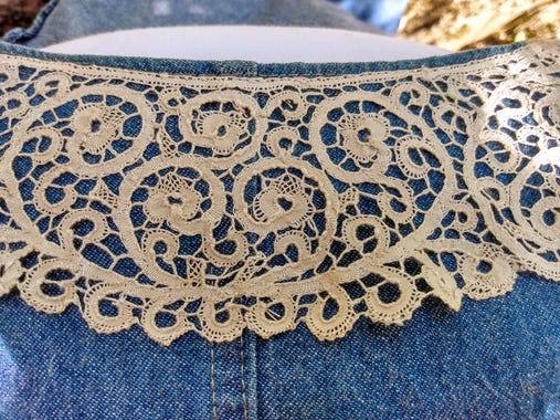 A beige linen Cantu lace collar, with scrolling paths and flowery motifs, attached to a denim jacket