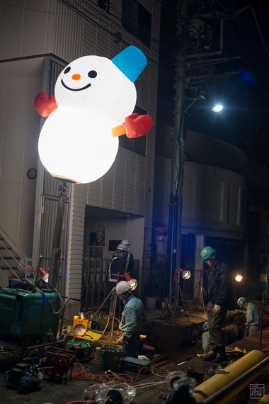 workers working at night under a lighting rig with an inflatable snowman diffuser