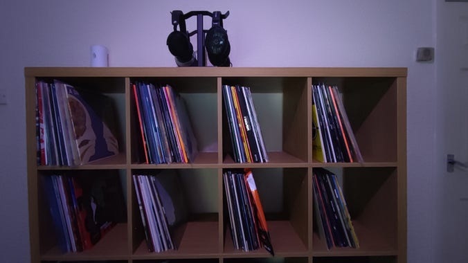 Top half of a 4x4 Kallax shelving unit showing records across them with headphones on stands above 