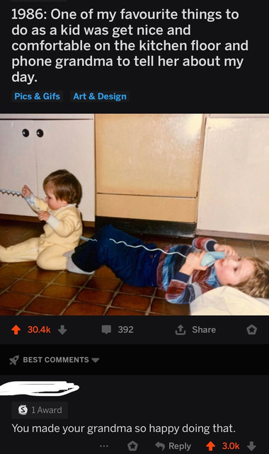 Old photo of a child lying down on the kitchen floor holding a telephone receiver with a long, spiralling cord, which is held by a baby. Caption: "1986: One of my favourite things to do as a kid was get nice and comfortable on the kitchen floor and phone grandma to tell her about my day." A reply reads: "You made your grandma so happy doing that."