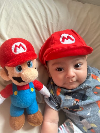 A cute baby in a Mario beanie next to a Mario plush