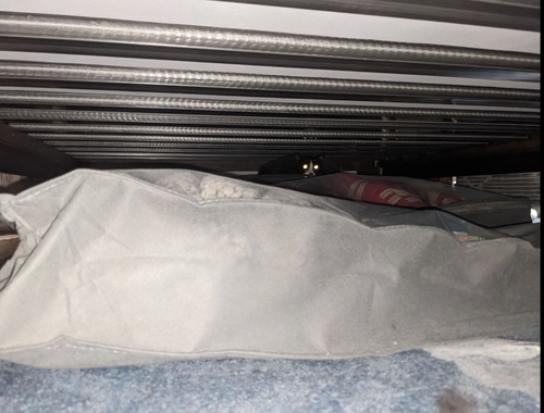 There is a cat deep under the bed. All that is visible is his bright, glowing eyes and a white stripe down his face.