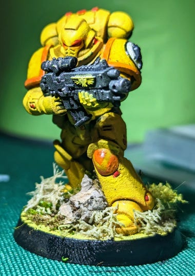 A painted Imperial Fists Intercessor Space Marine miniature with orange (6th company) markings and a bolter