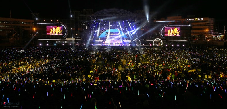 View of a stadium performance stage at night with thousands of people watching