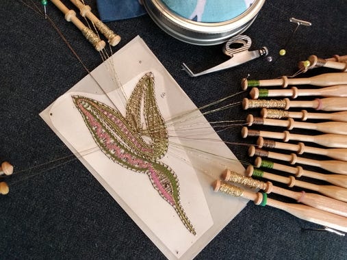 Hummingbird made in Milanese lace, in progress, with silk thread on bobbins all around the work