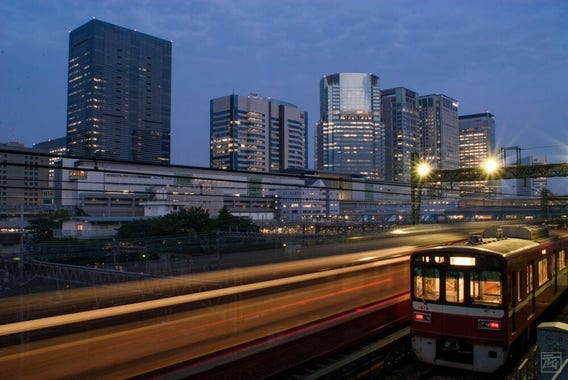 a blur of a train passes a parked train in front of the Shinagawa skyline