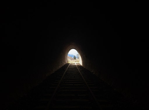 Image of a dark railway tunnel with the exit centered in the mid distance