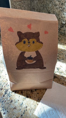 A brown paper, lunch bag with a little drawing of a cute squirrel, with several hearts above it holding an acorn