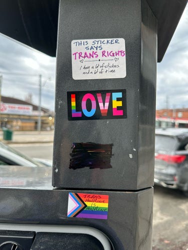 Parking meter with a pride sticker blotted out by sharpie. I added 2 more Pride stickers plus one that says “this sticker says trans rights… I have a lot of stickers and a lot of time”