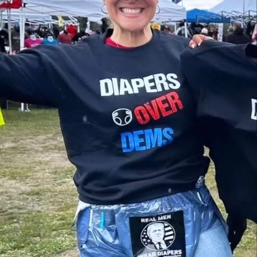 A female body (head cut off above the mouth) wearing a long sleeve, navy blue tee shirt that says "Diapers over Dems"
