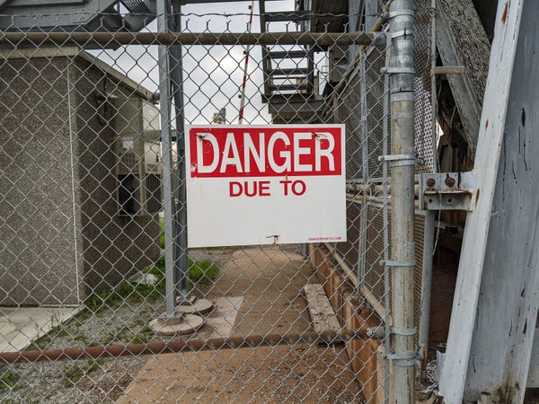 exterior day sign posted on a chain link fence: "DANGER DUE TO __________"
