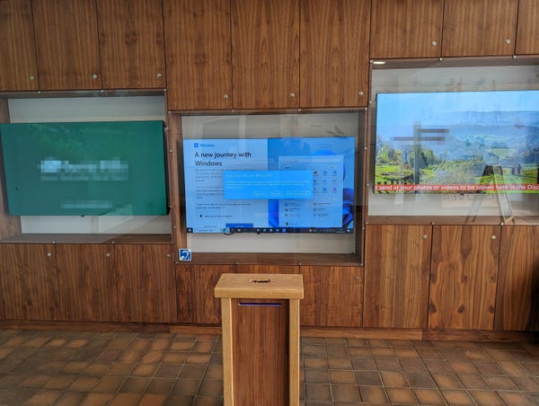 An exhibit of three massive displays, the middle display should be showing something interesting. Instead Microsoft have plastered a windows update box and an "upgrade to windows 11" offer over the normal display.
Some areas of the photo have been pixelated for privacy.