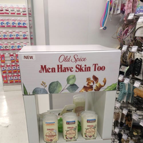 A cardboard stand of antiperspirant in a drugstore aisle. It says at the top "Old Spice: Men Have Skin Too".