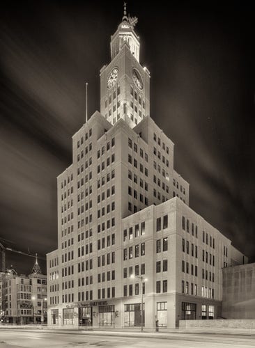 An early 20th century office building, with clock tower, at night.