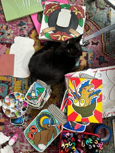 Black cat sitting amongst a lot of art 