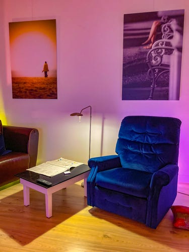 A blue chair next to a coffee table. There are two large photographs hanging on the wall. 