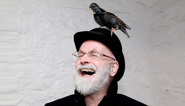 Sir Terry Pratchett, smiling, with a bird on his head.