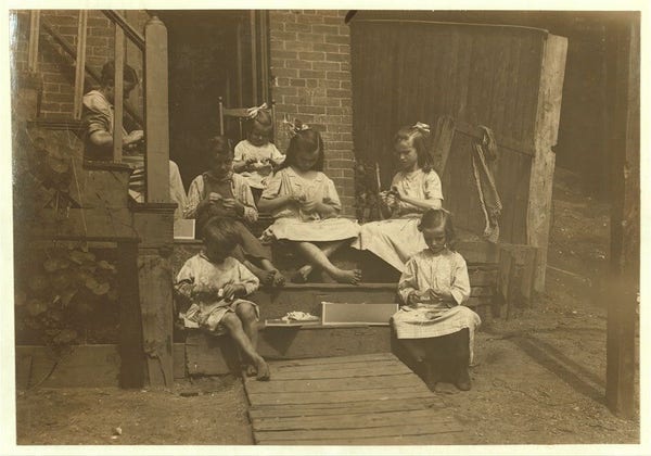  This is a historical black and white photograph featuring a group of children sitting on wooden steps. There are six children in the picture, ranging in age from young to teenagers. They appear to be engaged in an activity together, as suggested by their focused expressions. The setting looks like it could be a family home, with a brick wall visible in the background and what appears to be a chair on the left side of the frame.

The image has a text overlay that reads "Family of Mrs. Donovan, 293 1/2 Highland Street, Roxbury, Mass., tying tags for Dennison Co." This indicates that the family was involved in making tags for an organization named Dennison Co. for seven years, and their work generated an average income of $30 per month. At one point, they made as much as $42 in a single month. The mother's concern about whether they would be able to continue this work is noted, along with the fact that all children aged 13, 9, 11, and 7, as well as twins who were four years old at the time, helped their mother. They often had to work late into the night to meet their deadlines. The image also has a reference to "Home Work report," which suggests it is part of a historical record or documentation related to home-based work and labor practices in the past.

For visually impaired users, this description provides information about the content of the photograph without relying on visual details that might not be clear due to th [...]