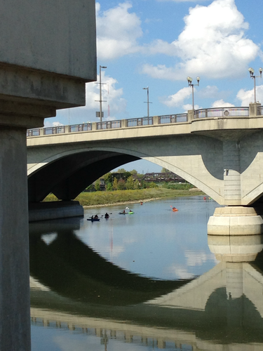 Colorful kayakers flowing on the gentle current under a white arched bridge in Columbus on a beautiful summer day. 