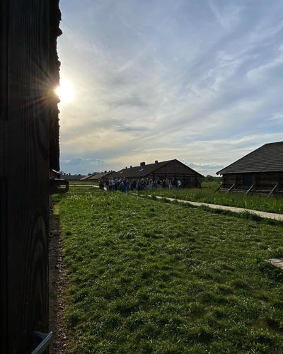 Brick barracks at the site of the former Auschwitz II-Birkenau camp. Sun visible in the sky. Between the barracks - some people, visitors of the Auschwitz Memorial.