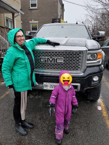 A photo of me (carrying a baby under my coat) and my 4-year-old standing in front of a GMC pickup truck. The hood is about a foot below my head.