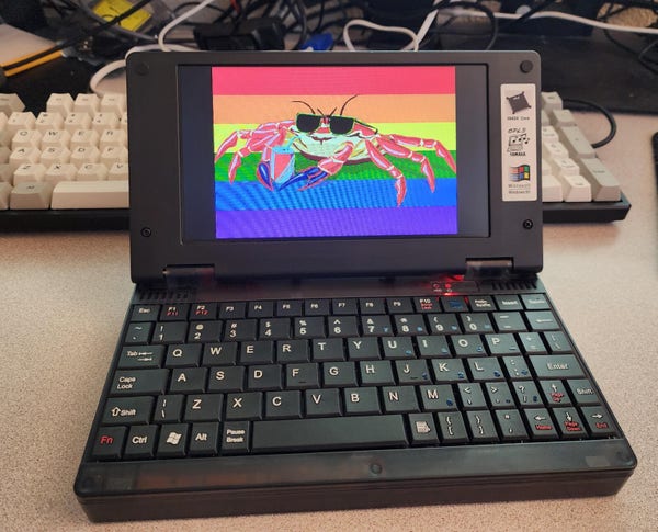 A small black Palmtop PC, with a compact keyboard and a 16:9 LCD screen.
It's displaying the Cool Crab Pride Flag 