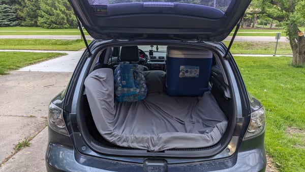 A Mazda 3 hatch with a mattress topper as a makeshift bed
