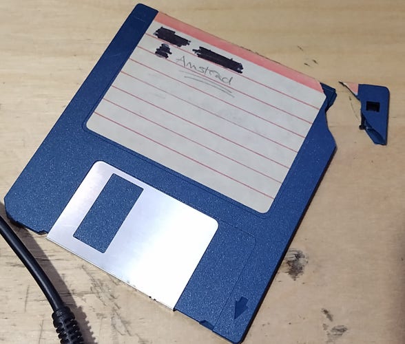 A blue floppy disk with a white, striped label which says "Amstrad" on it. The top right hand corner has broken off.