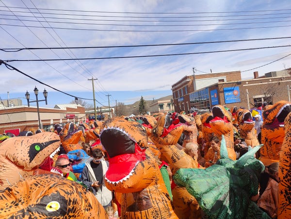 A street level view of a lot of people in dinosaur costumes from Drumheller Alberta on 2024-04-27