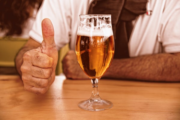 Someone giving a thumbs up next to a glass of pale beer